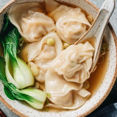 A bowl of wonton soup with pork and shrimp wontons, baby bok choy, and green onion in clear broth