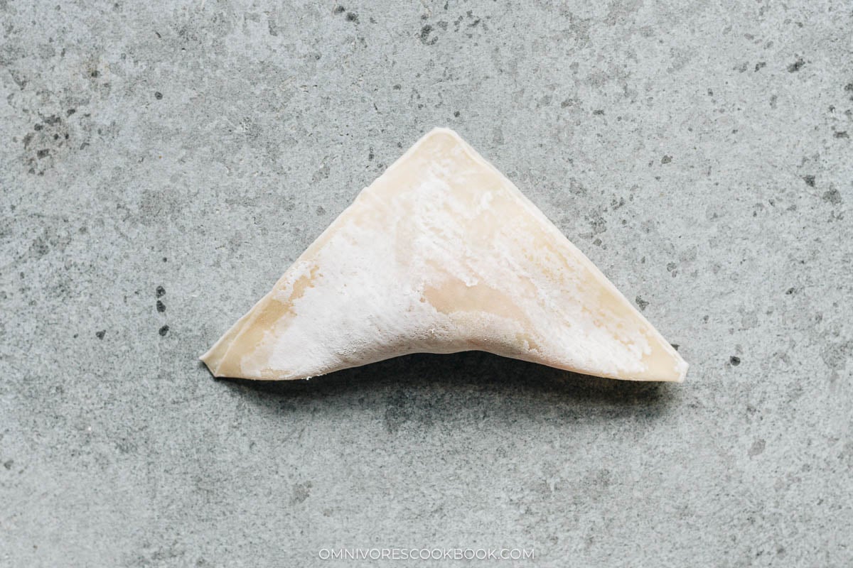 Folding a wonton wrapper into a triangle over the filling and pressing out the air