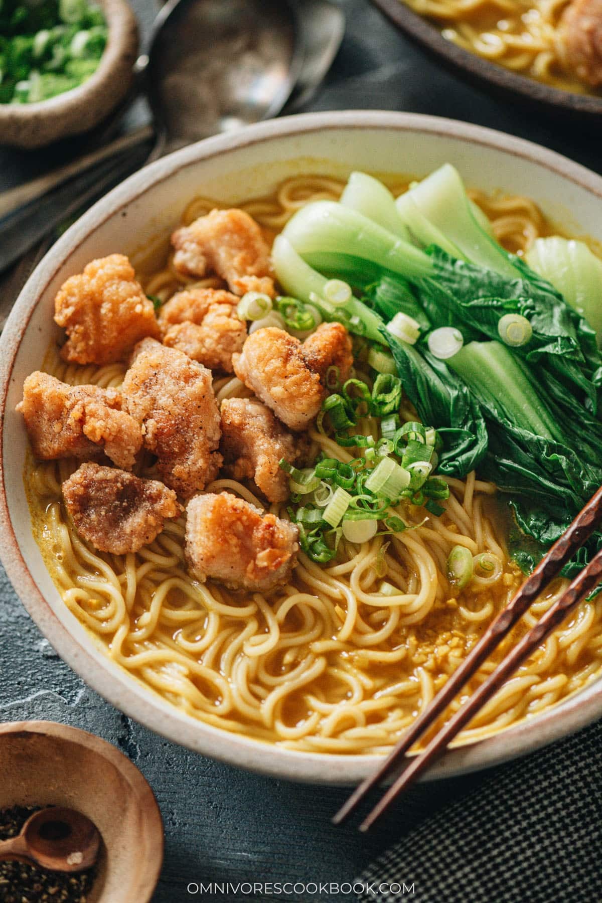 Bowl of curry noodle soup topped with crispy popcorn chicken, baby bok choy, and green onion
