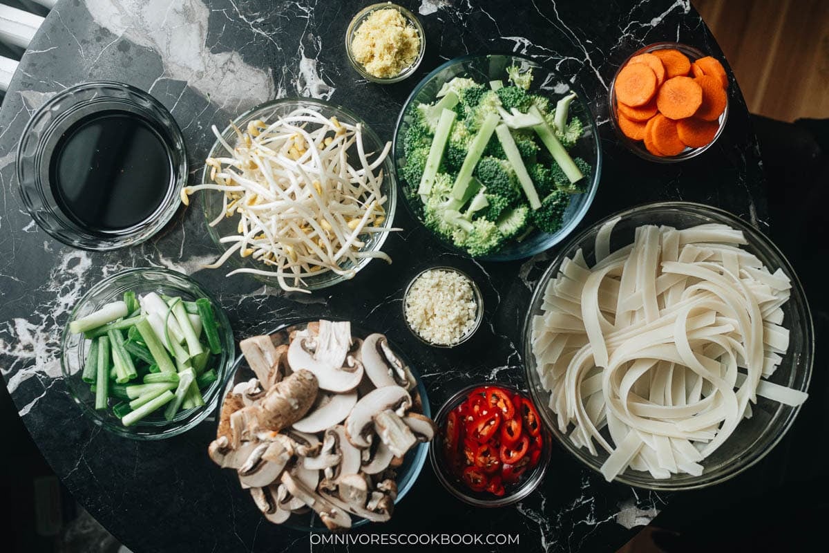 Ingredients for vegetable chow fun grouped as rice noodles, sauce, and fresh vegetables