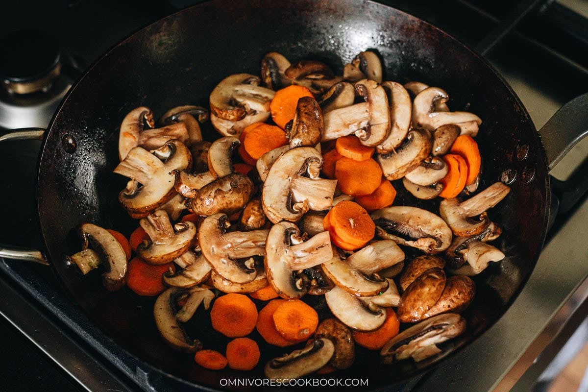 Sliced carrot and button mushrooms browning in oil in the skillet