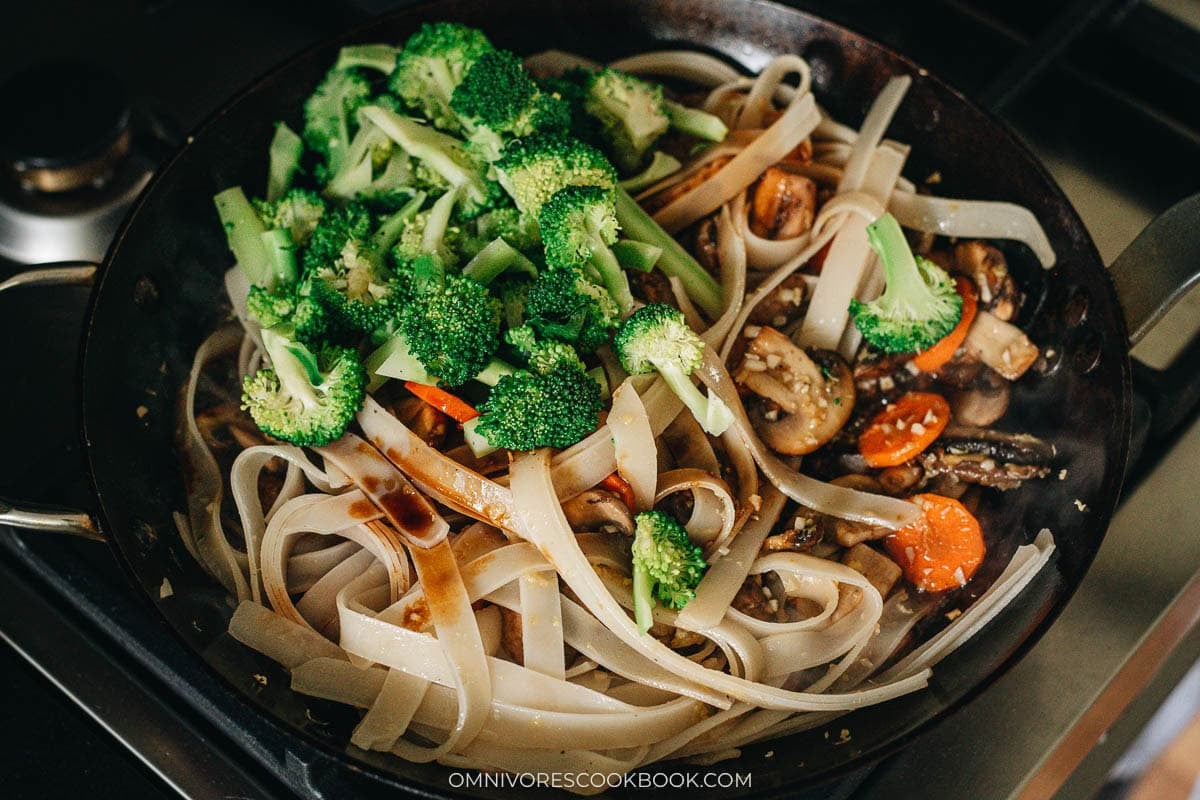 Wide rice noodles and broccoli tossed with the dark sauce in the skillet