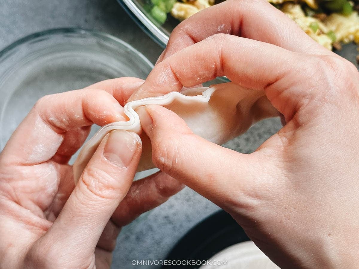 Folding egg and pepper dumpling filling into a wetted wrapper by hand