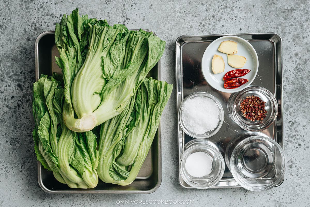 Fresh mustard greens, pickling salt, ginger, dried Chinese chilies, Sichuan peppercorns, and baijiu laid out for pickling