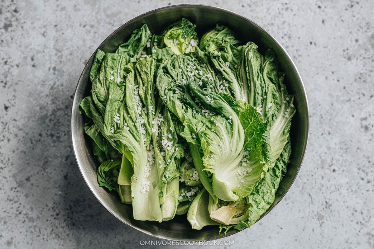 Salt rubbed into mustard greens in a large bowl to coat the leaves